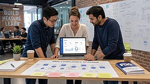 Startup team collaborating around a laptop showing cloud QMS software in a modern co-working space with quality compliance roadmap materials